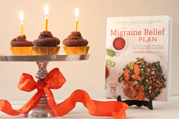 Cupcakes on a cake stand with lit candles and The Migraine Relief Plan book
